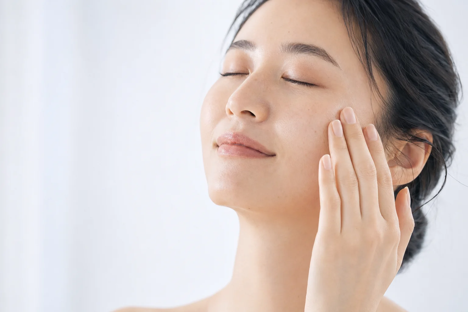 A woman with a clear, even complexion resting her fingertips at her cheekbone