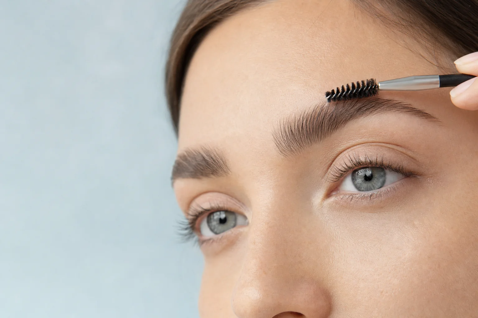 A spoolie brush combing through a full, softly groomed brow