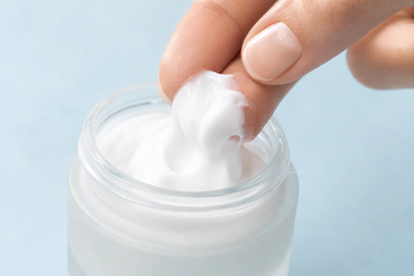 Fingertips scooping moisturizer from a jar